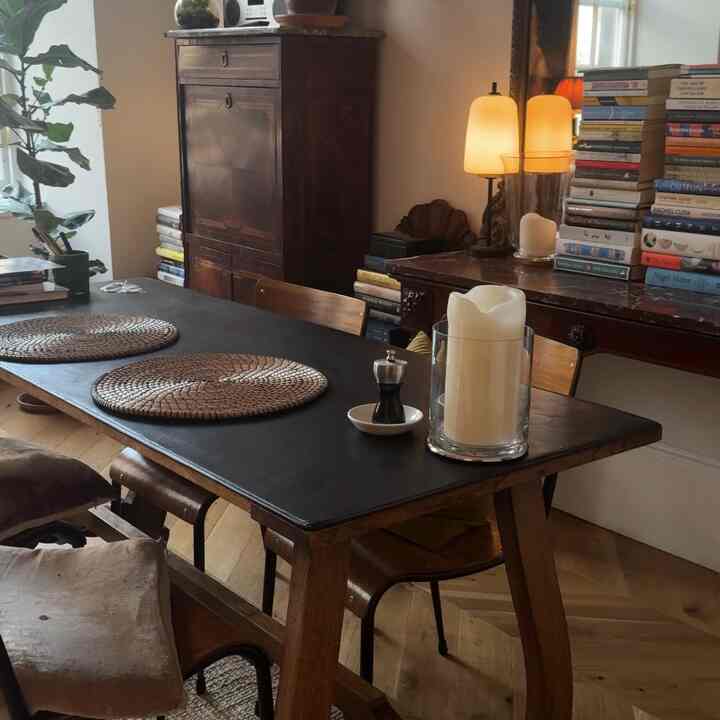 Art Deco dining room with dark brown wood tones, vintage furniture and stacked books, featuring candles creating a warm atmosphere
