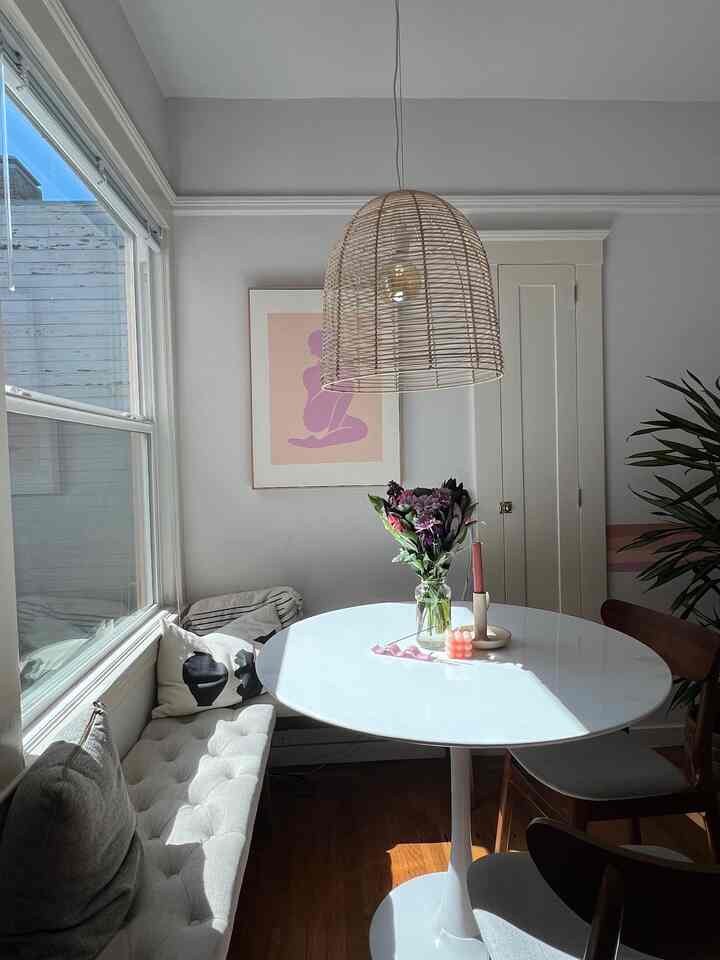 White and natural toned dining room featuring a round dining table, bench, and rattan pendant light creating a cozy atmosphere