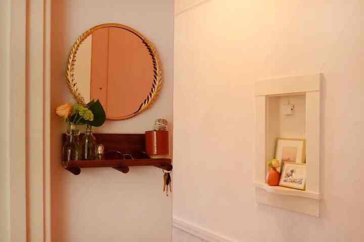 Beige-toned small entrance featuring wood tone shelf, gold leaf mirror, peg hooks, and vases arranged in a minimal style