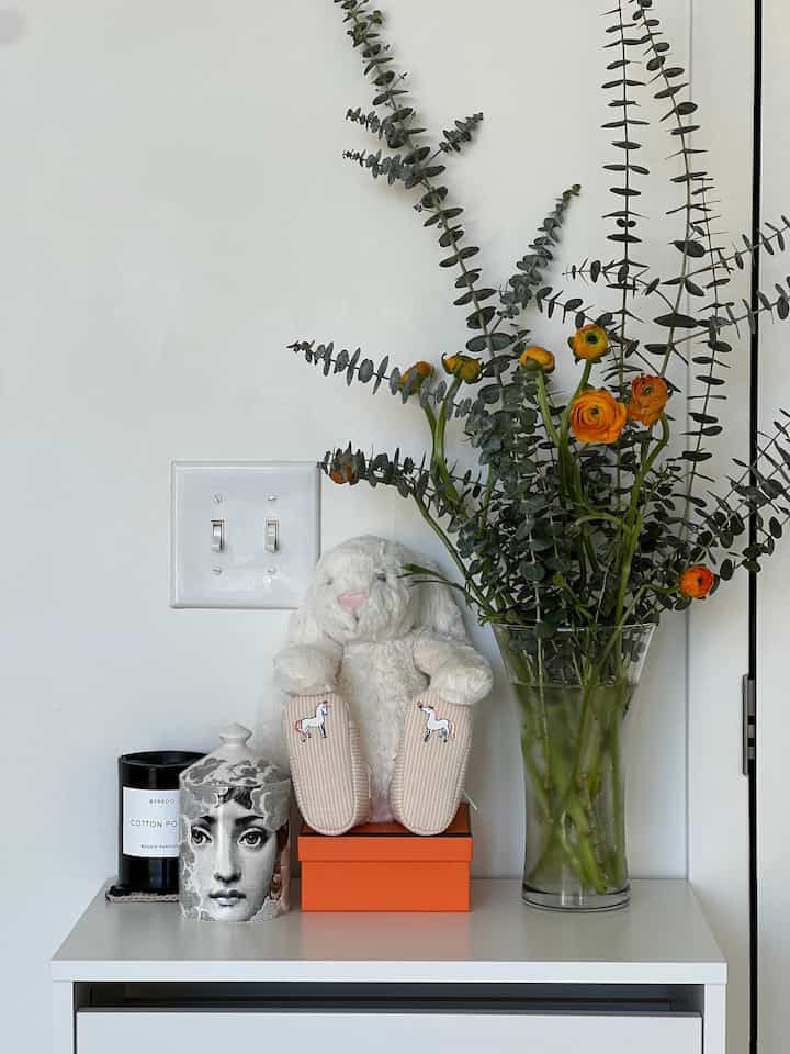 Bright white-walled entrance featuring a white shoe cabinet, transparent vase with orange flowers and green eucalyptus creating a cozy atmosphere