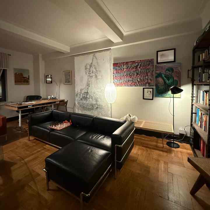 Mid-century modern living room with black leather sofa, wood-toned flooring, and floor lamps creating moody lighting