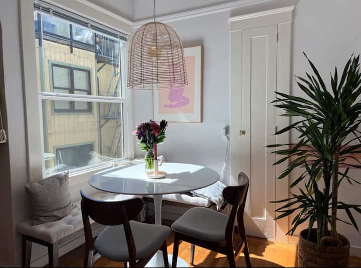 Modern two-person dining room in white and wood tones, featuring a round dining table with bench and chairs creating a cozy corner