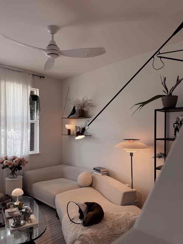 Ivory and beige toned living room featuring a beige sofa, floor lamp, and wall shelves, creating a cozy atmosphere