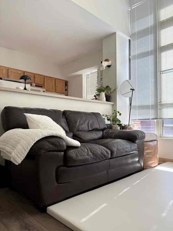 Bright white-toned living room featuring a brown leather loveseat near large windows, creating a cozy small space