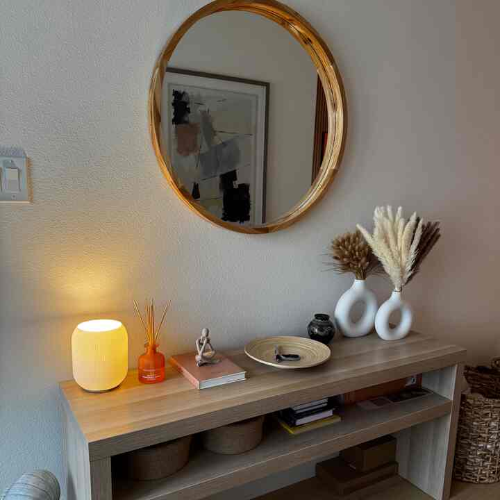 Natural-toned entrance featuring round wooden mirror, console table, and warm table lamp with cozy atmosphere