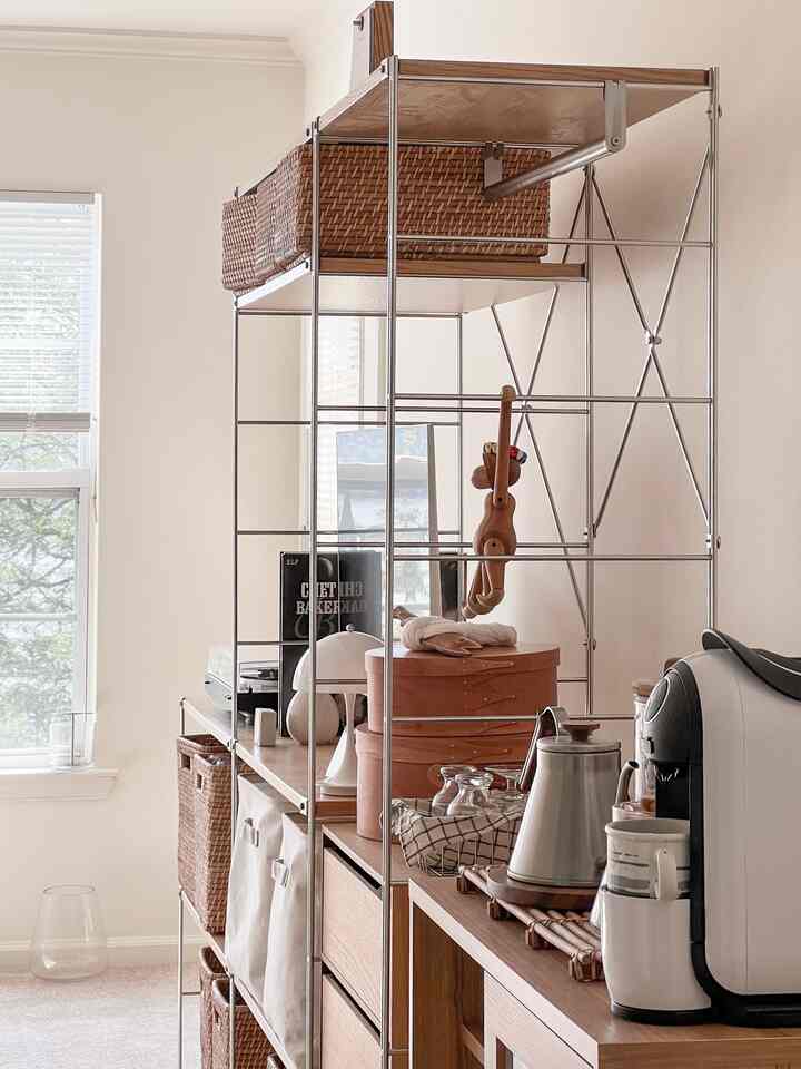 Natural beige-toned room with metal shelving and wood-tone cabinet featuring coffee machine and storage baskets creating cozy home cafe vibe