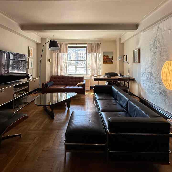 Brown and black toned mid-century modern living room featuring sofas, wooden coffee table, and desk by the window creating cozy atmosphere