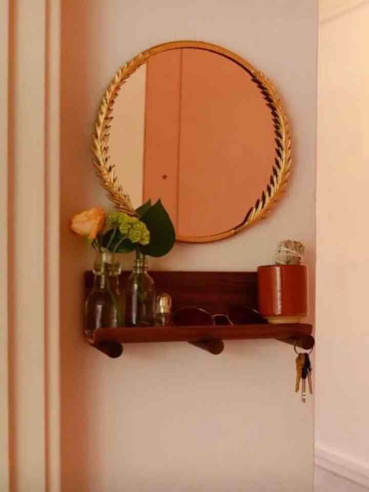 Cozy entrance space featuring brown wooden shelf and round golden mirror with minimalist decor