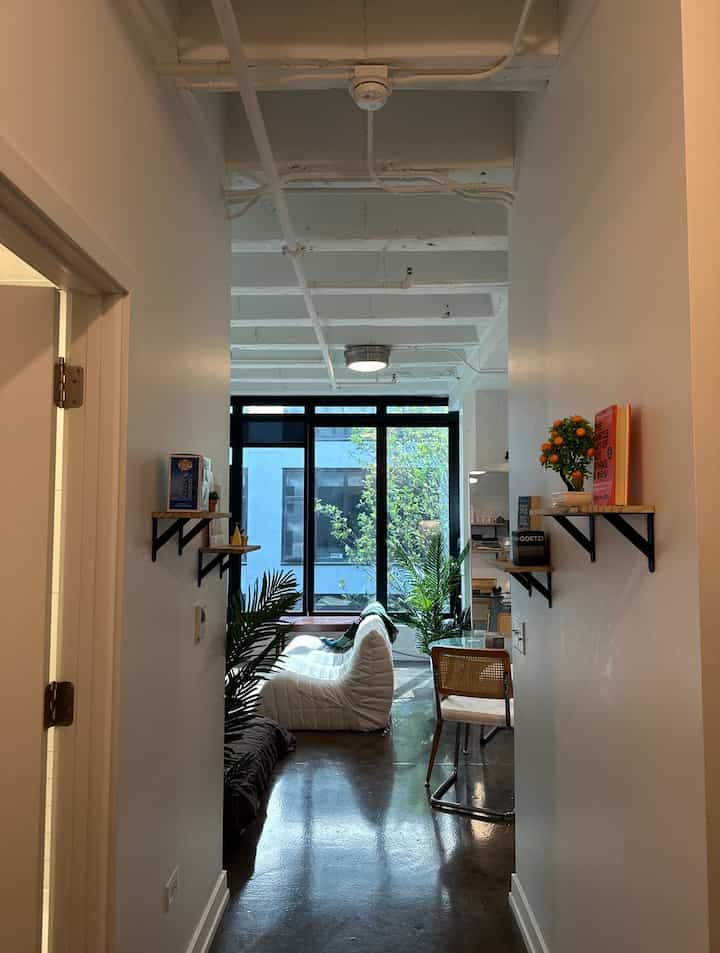 Bright white and natural wood-toned narrow entrance featuring mid-century modern furniture and lush plants for a cozy ambiance