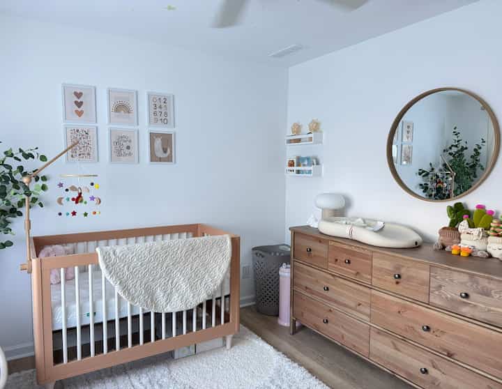 A bright white and beige baby room featuring a natural wood dresser and crib, creating a clean and warm atmosphere