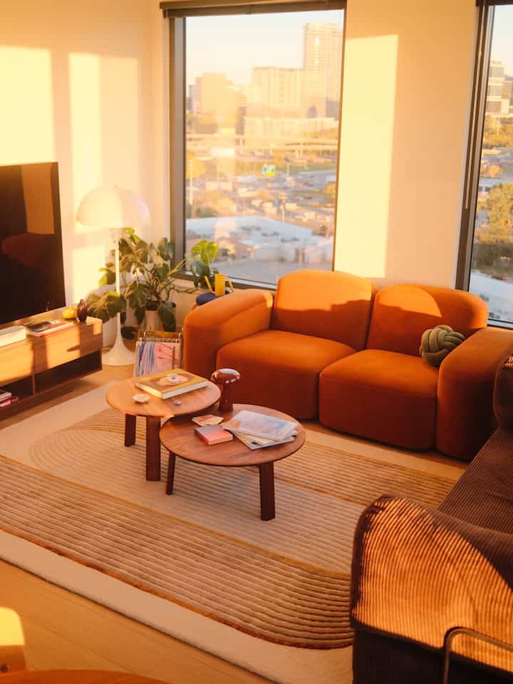 A warm wood tone urban apartment living room featuring an orange sofa bathed in sunlight creating cozy atmosphere