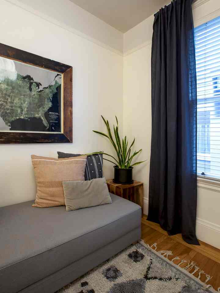 Gray and blue toned home office corner featuring a sofa bed, wooden side table, and potted plant creating a cozy atmosphere