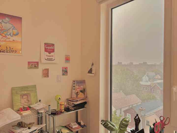 Cozy home office space with beige-toned walls and a metal shelf, rainy cityscape visible through the window