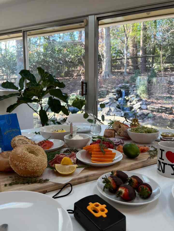 Bright white-toned dining room featuring a Saarinen dining table centrally placed, set with bagels and assorted brunch dishes creating a home cafe vibe