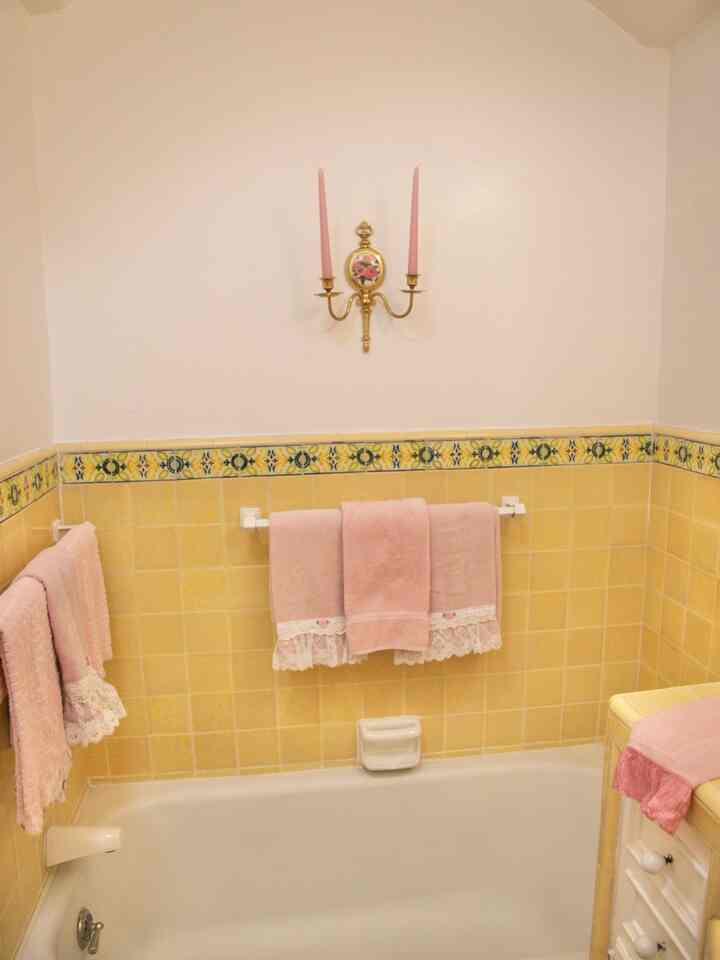 Bathroom space with yellow tiled walls, vintage pink towels, and pink decorative wall candles