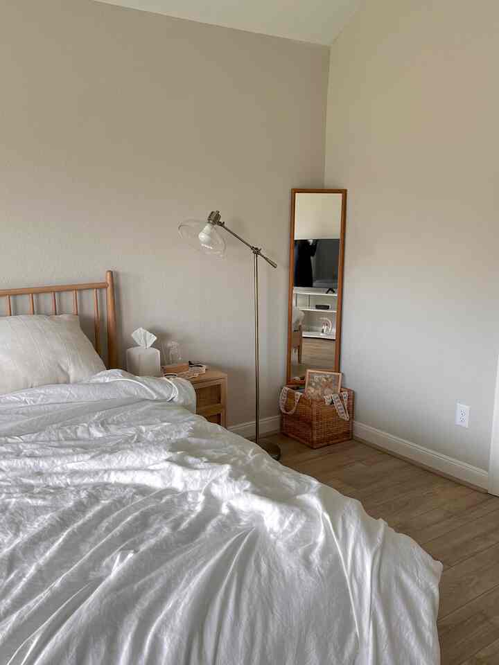 Natural white and brown toned bedroom featuring mid-century modern furniture, floor lamp, and full-length mirror with cozy atmosphere