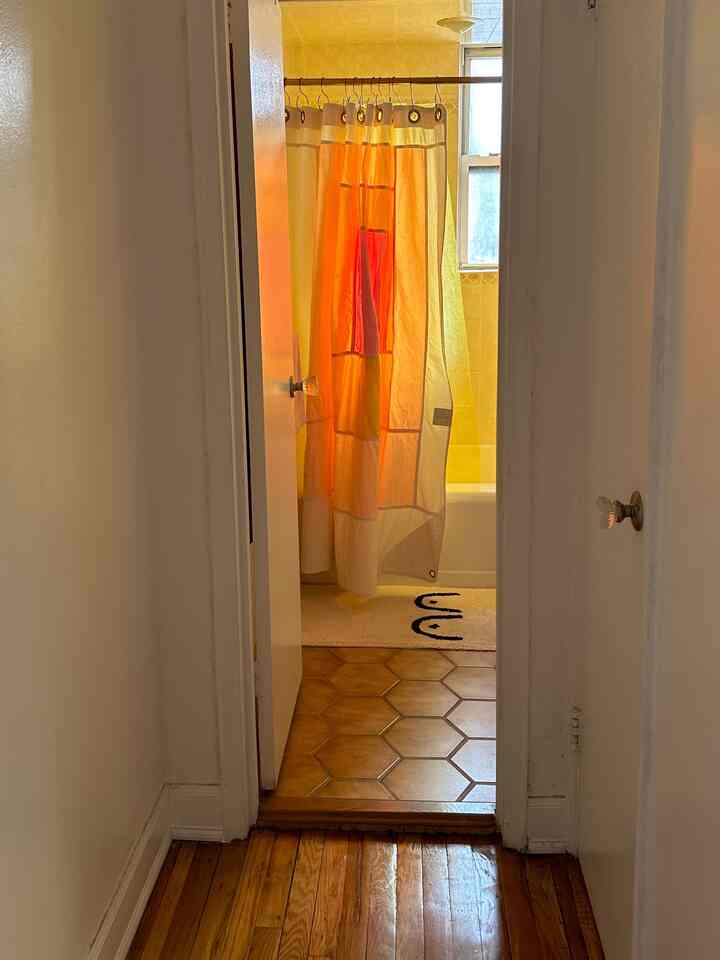 A modern bathroom with yellow tiles and a white bath mat visible through a corridor