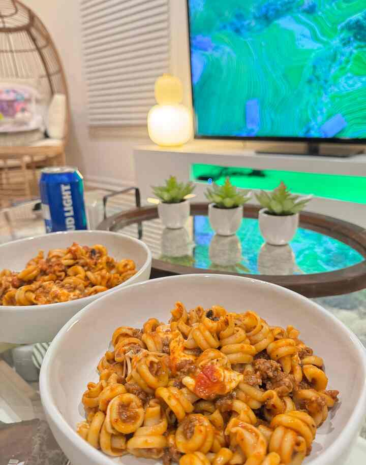 White-toned living room featuring a round glass table with pasta bowls and mini plants, creating a cozy atmosphere