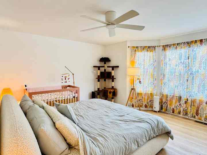 Light gray bedding and natural wood tones of baby crib and cat tower in a warm, cozy bedroom space
