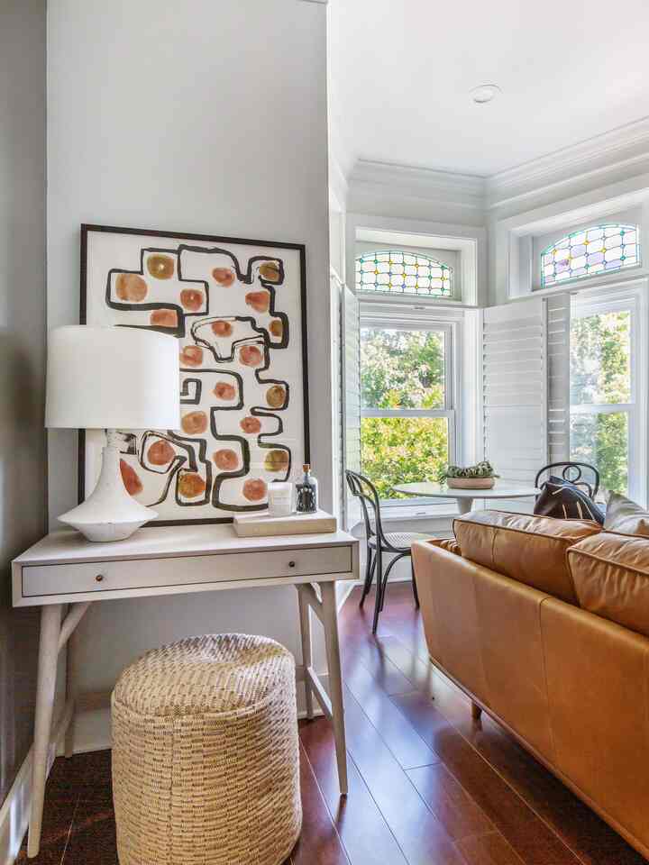 Bright white walled living and entrance area with wood tone flooring, featuring leather sofa, mid-century mini desk and table lamp in warm atmosphere