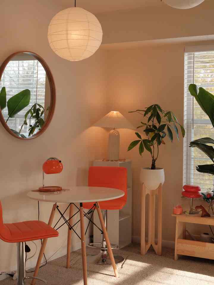 Natural modern dining room with soft orange bar stools repurposed as chairs, white round dining table, plants, and warm lighting