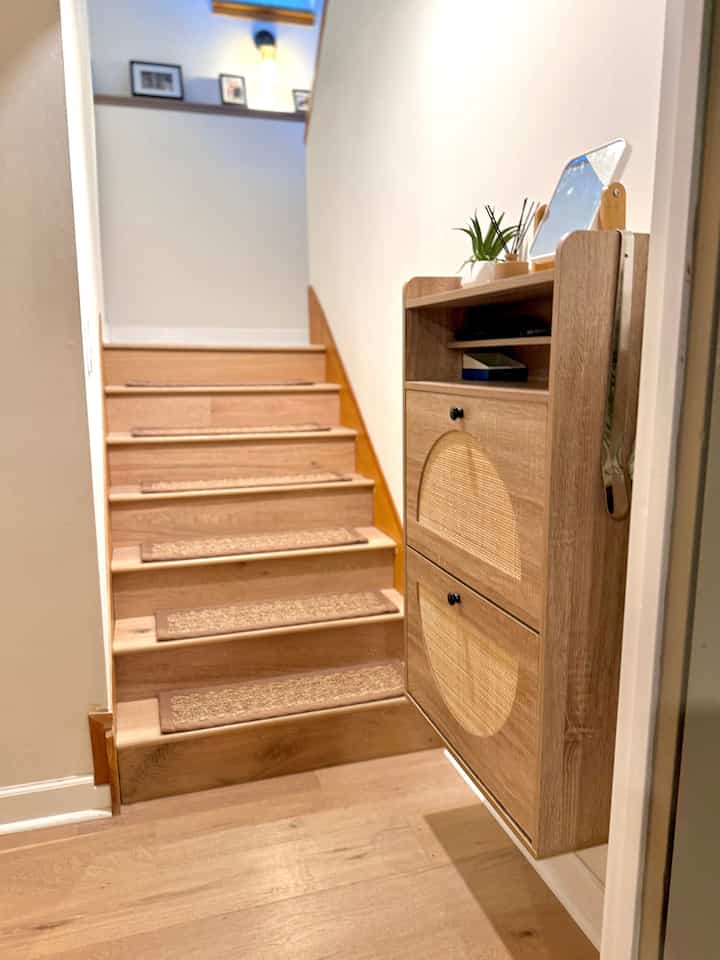 Bright wood-tone floor and staircase with rattan shoe cabinet arranged in a modern entrance space