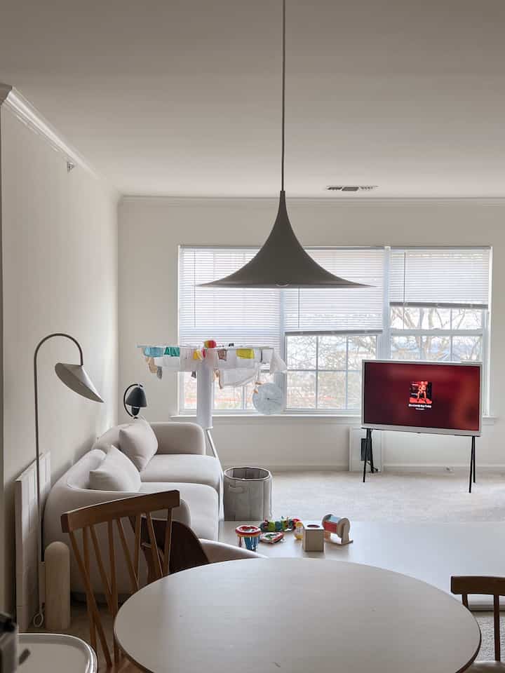 Beige-toned living room featuring white sofa, round coffee table, baby toys and a clock in a soft natural setting