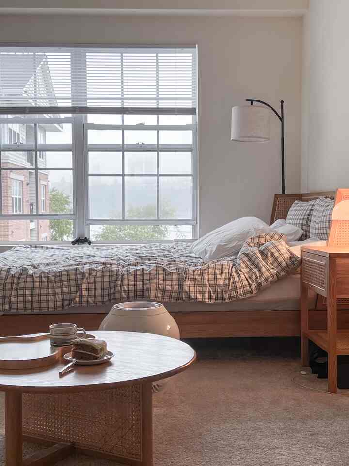 A cozy bedroom in natural wood tones featuring a large window and round coffee table with soft lighting
