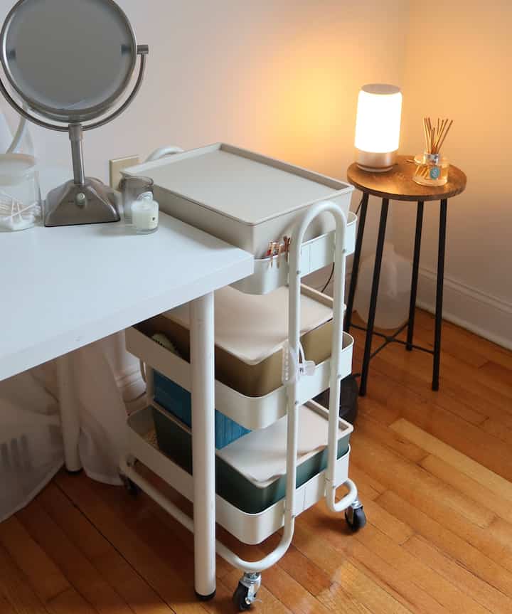White and wood-toned vanity space featuring a tidy storage cart and soft lighting creating a cozy atmosphere