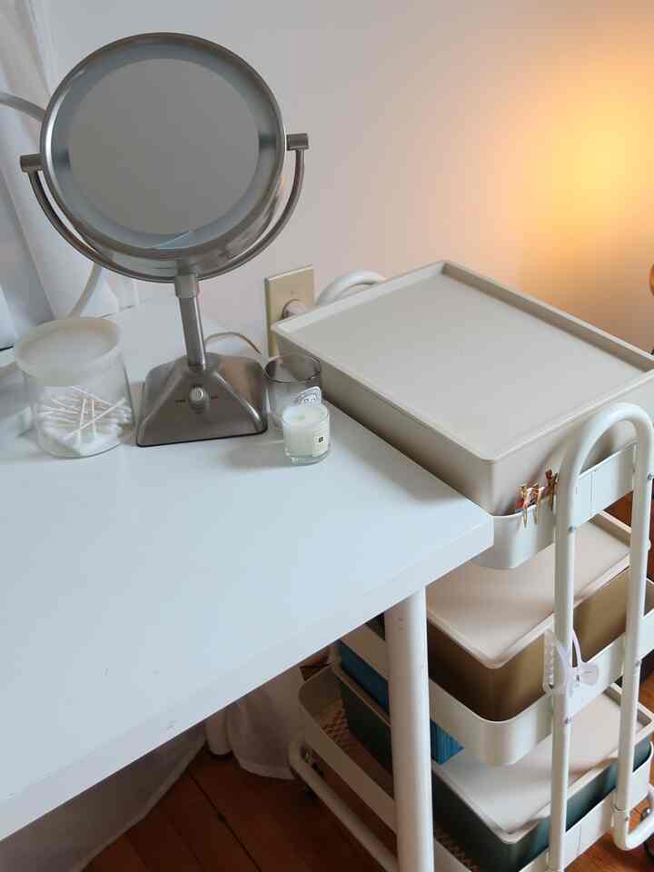 White and cream toned powder room featuring a vanity table with a standing mirror and a 3-tier storage cart, minimalistic and tidy setup