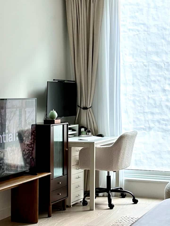 White and beige toned home office space with desk and chair positioned by window, creating a bright and tidy atmosphere