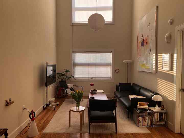 Beige-walled modern living room with wood tone floor, featuring a black leather sofa and wooden coffee table creating a cozy atmosphere