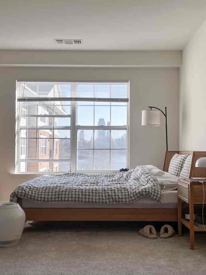 White and wood tone bedroom featuring check-pattern duvet, nightstand, and floor lamp in a cozy space