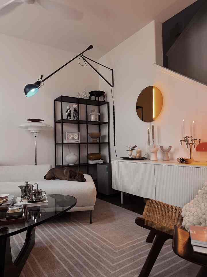 A beige and white toned living room featuring simple modern furniture with a dog resting on the sofa creating a cozy atmosphere