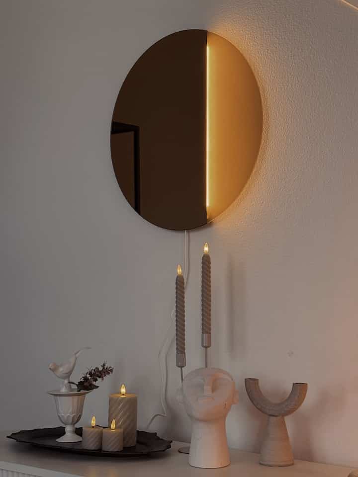 Warm natural-tone living room featuring a round mirror, wall lamp, candles, and sculptural objets stylishly arranged