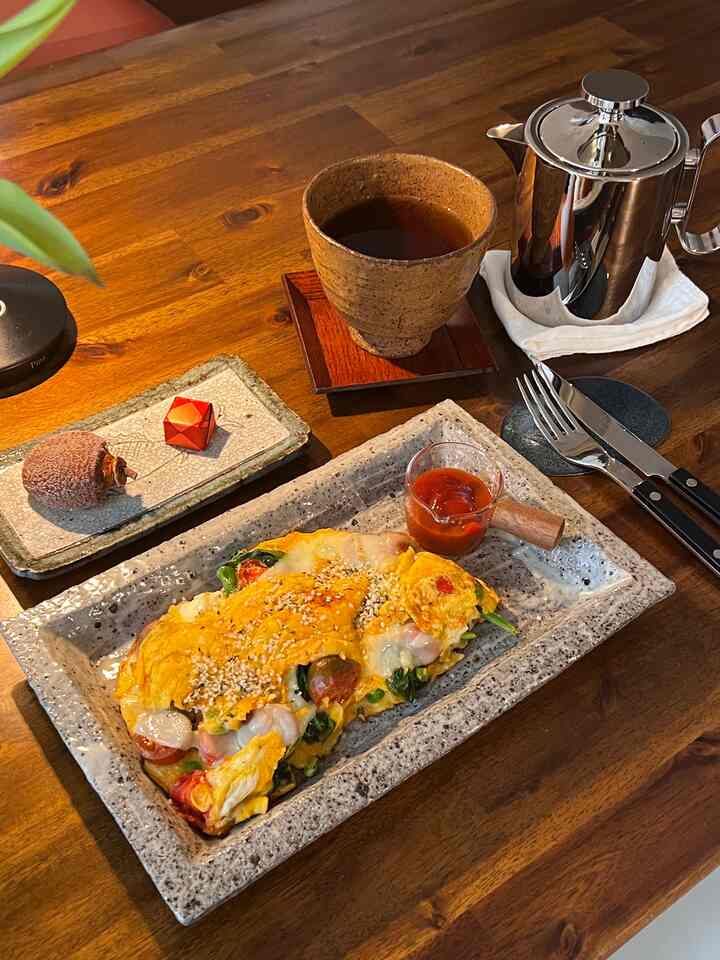 Cozy meal setup on warm brown wood table featuring a home cafe style omelette on a plate with stainless steel teapot and cutlery