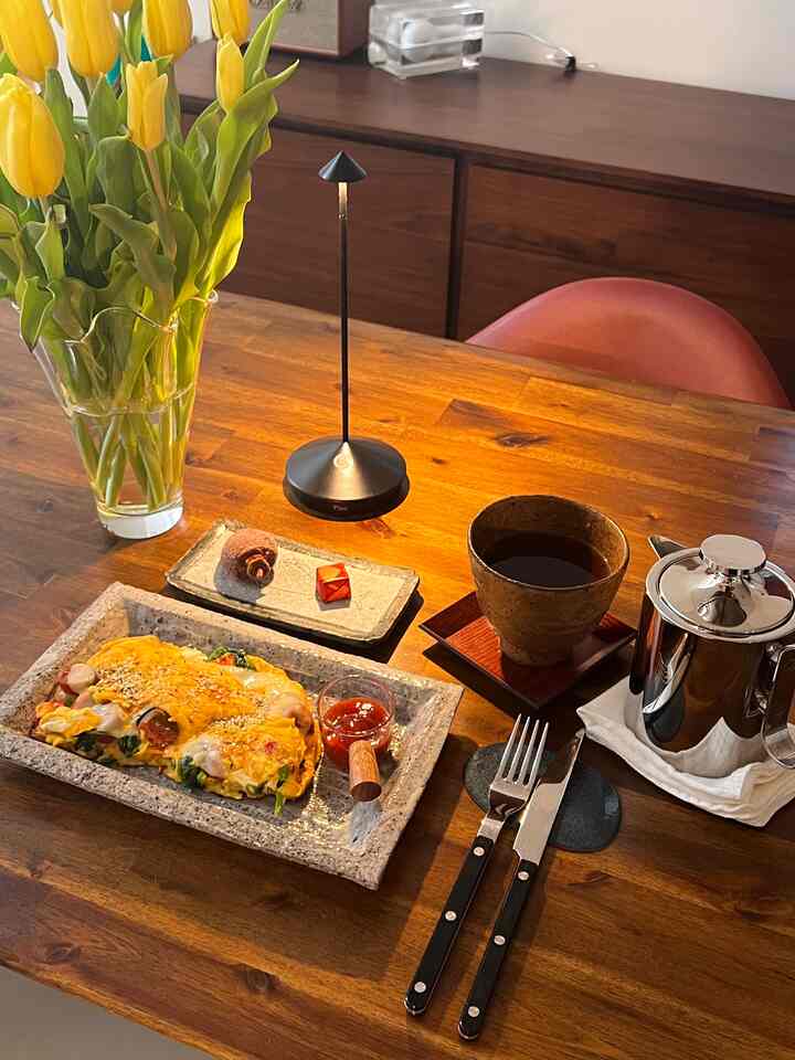 Warm brown toned kitchen dining table featuring French cutlery, table lamp, coffee, and omelette in a cozy home cafe setting