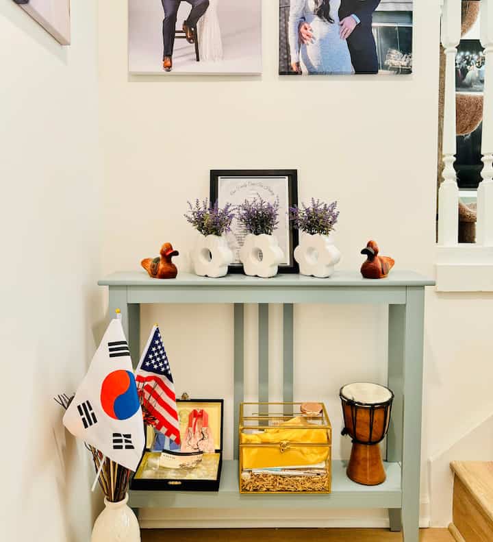 Ivory walls and mint green console table in a stair entrance corner featuring vases and decorative items creating a cozy space