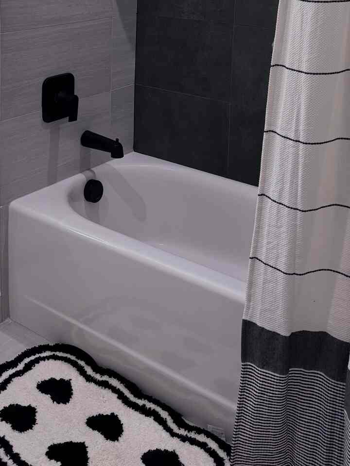 Black and white bathroom featuring a white bathtub, striped shower curtain, and a heart-patterned rug with a modern vibe