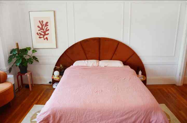 Modern studio bedroom with pink bedding and brown Almelo headboard, natural wood floor and white walls creating warm atmosphere
