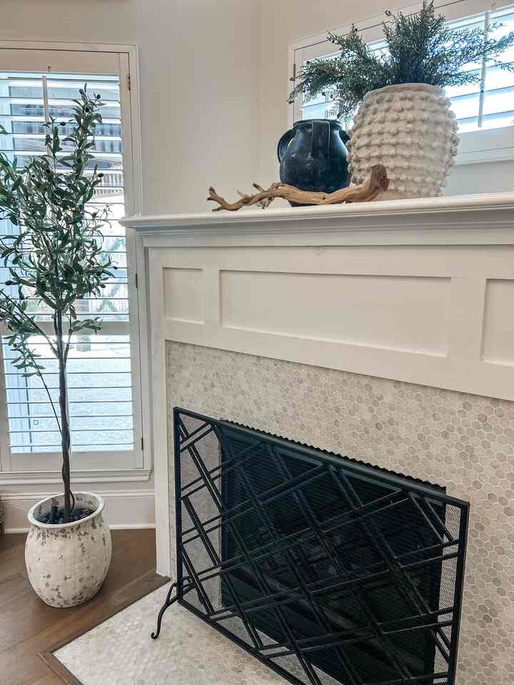 White and natural toned living room with large vases on fireplace mantel and plant stand, creating a cozy atmosphere