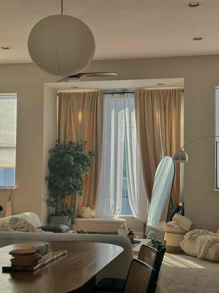 Natural color toned living room featuring a rice paper pendant light, wooden dining table, floor lamp, and soft curtains creating a cozy atmosphere