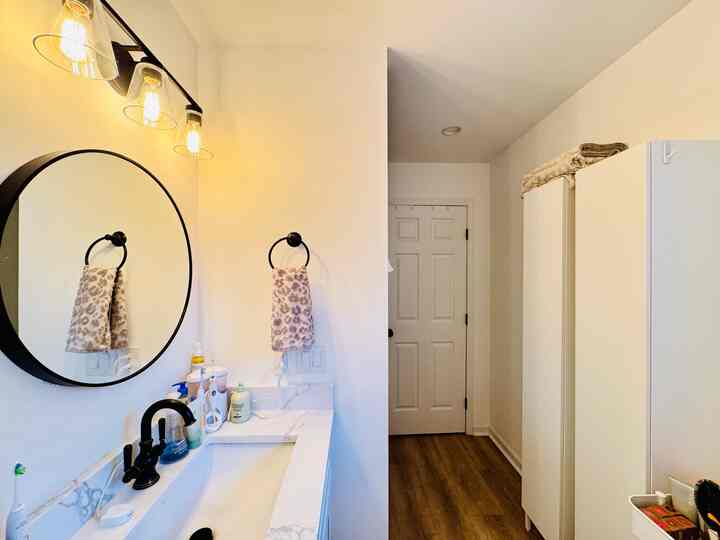 White and black bathroom featuring a round mirror and towel ring, with clean countertops and modern style