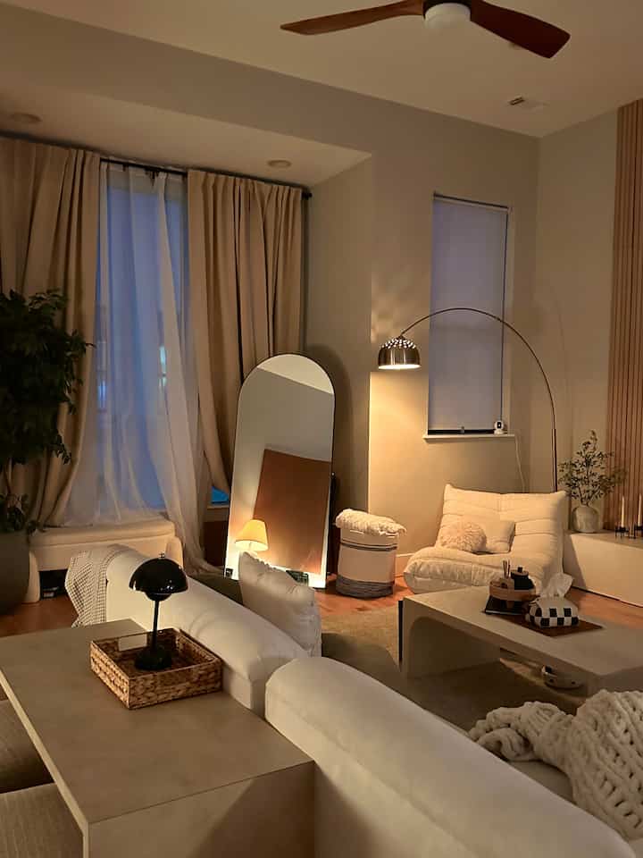 Beige and wood tone living room featuring cozy sofa, arched mirror, and warm lighting with comfortable ambiance