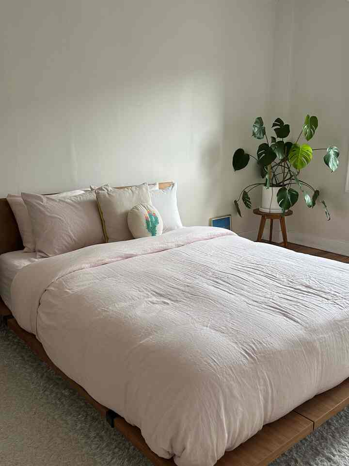 Bright natural-toned bedroom featuring a wooden bed frame and light pink bedding in a minimalist setting
