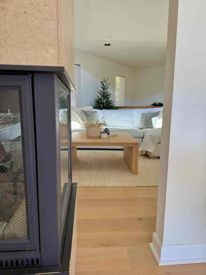 A bright white and natural wood tone living room featuring a sofa and coffee table with a modern, clean atmosphere
