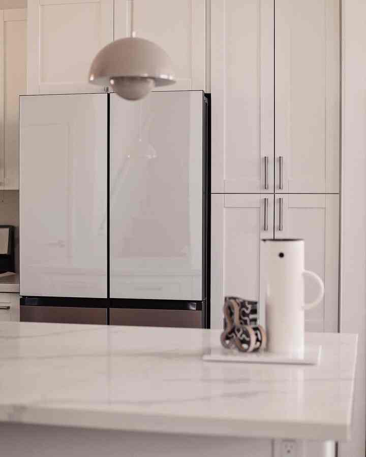 White-toned kitchen featuring a Samsung refrigerator and marble countertop with a Stelton pitcher and napkin holder in a clean, minimal Japandi style space.