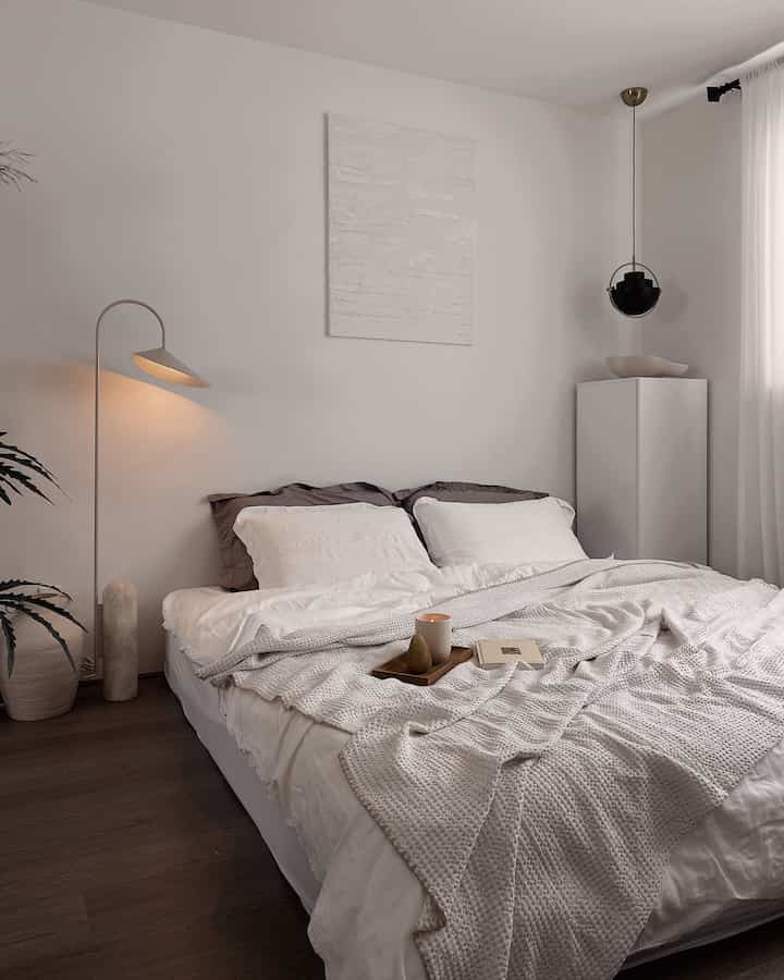 White and beige toned bedroom featuring a large central bed with minimal lighting, creating a natural and cozy atmosphere