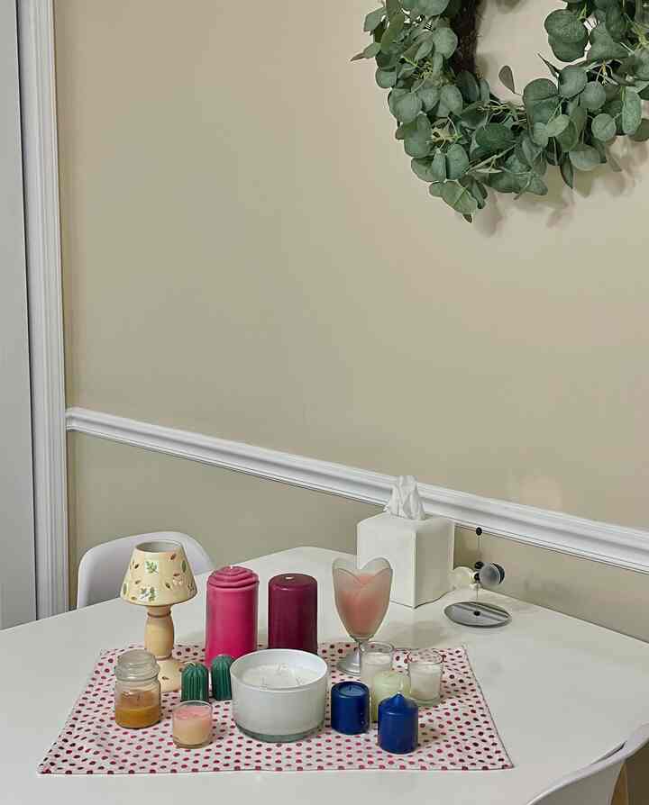 A simple natural dining room with white table and chairs, featuring an arrangement of candles on a pink polka dot table runner