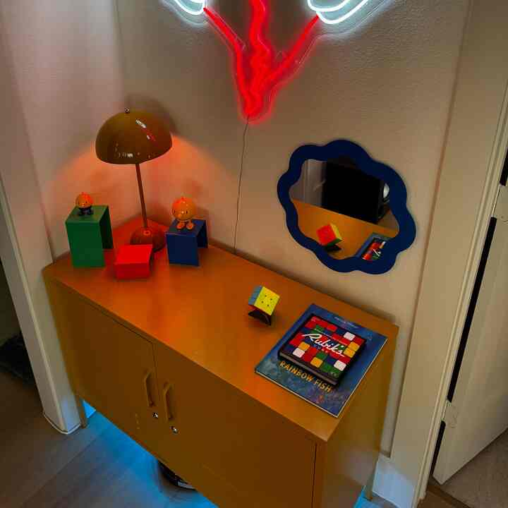 Playful corner with a yellow locker-style cabinet, blue-framed wavy mirror, and yellow table lamp creating a colorful atmosphere